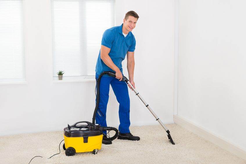 44713298 - happy male janitor cleaning carpet with vacuum cleaner